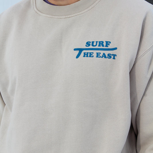 Beige sweatshirt with blue 'Surf The East' text on it.