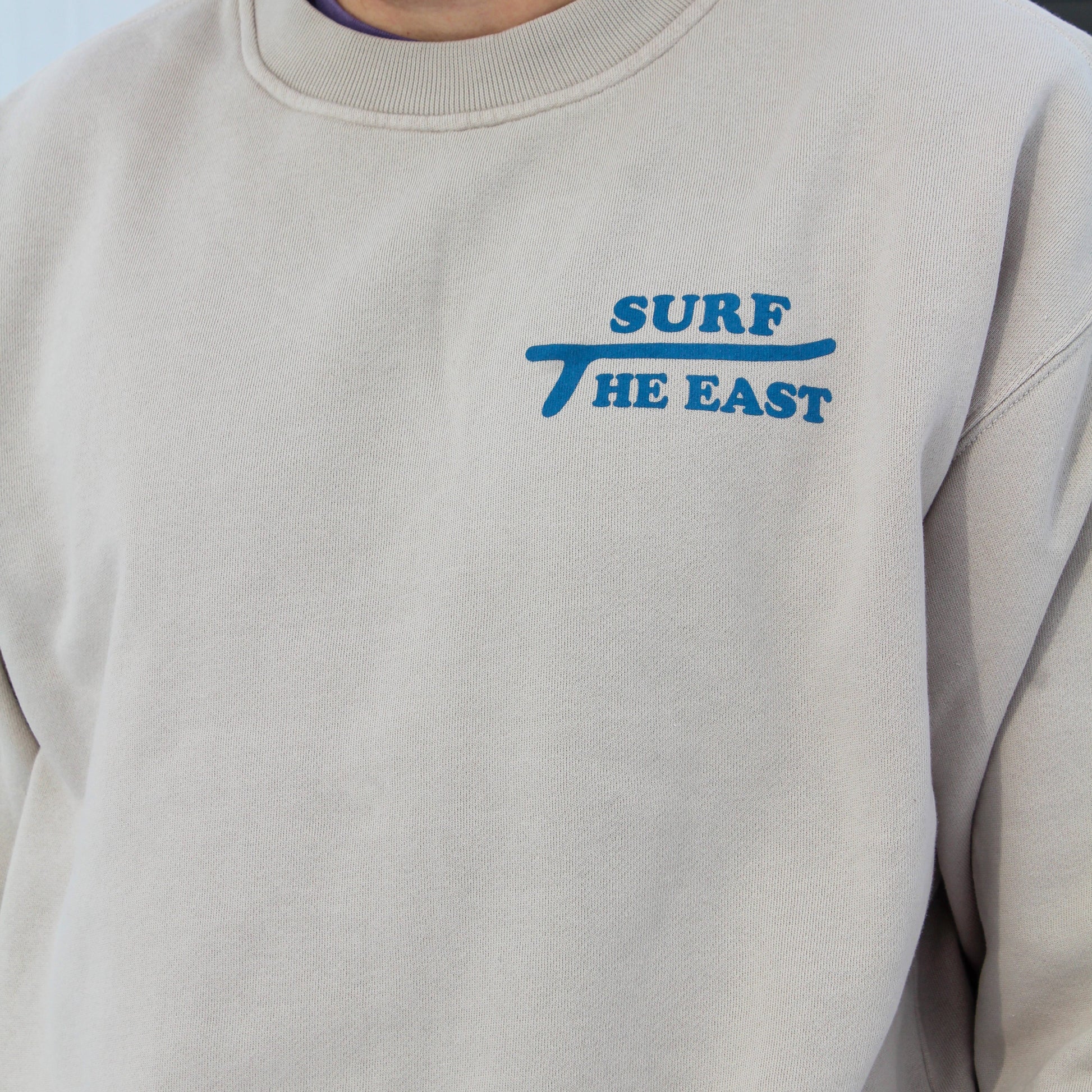 Beige sweatshirt with blue 'Surf The East' text on it.